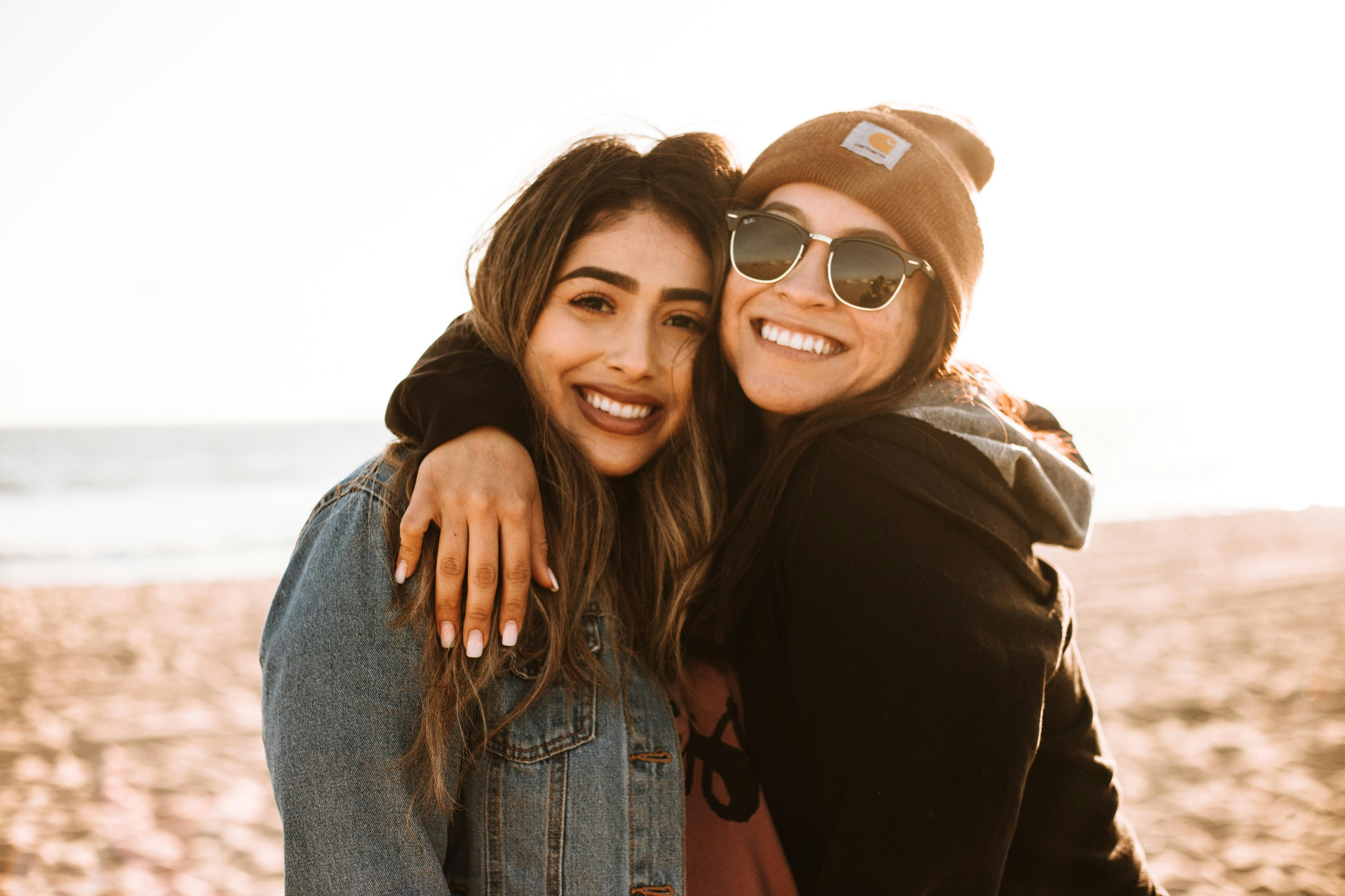 Portrait of Daniela Ortiz, a PeerCaster in a denim jacket, smiling with a friend on a sunny beach