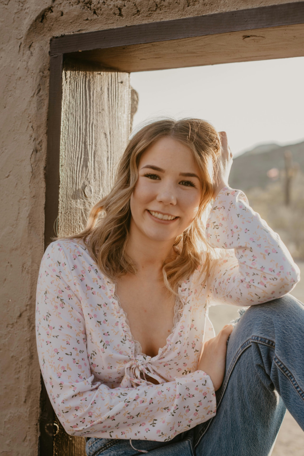 Portrait of Marisol Reyes, a PeerCaster with long wavy blonde hair, smiling against a weathered adobe wall in golden light