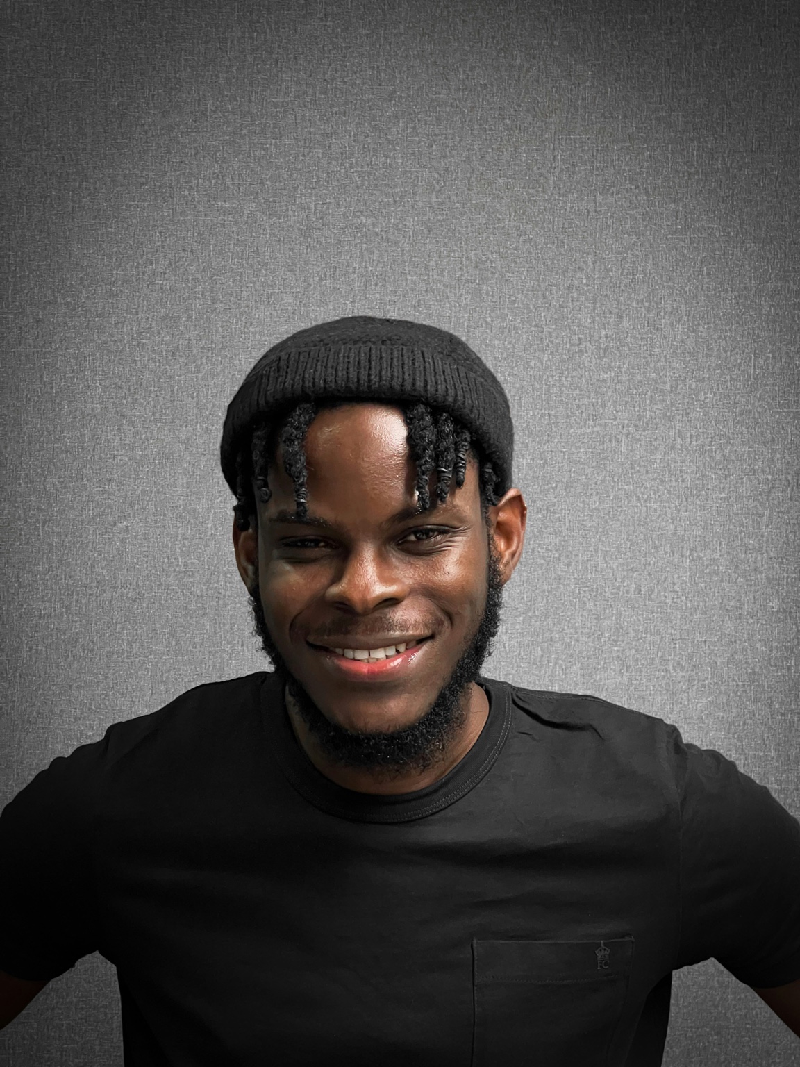 Portrait of Andre Whitfield, a PeerCaster in a black beanie and black t-shirt, smiling against a plain grey wall