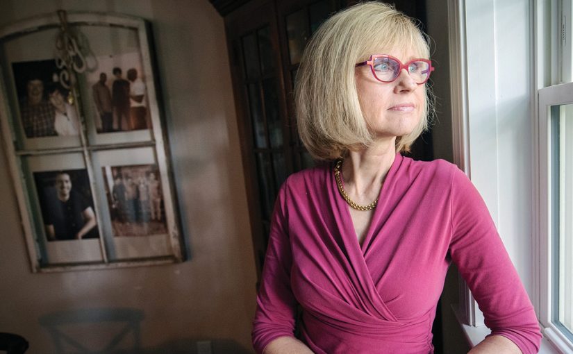 A woman in pink looking thoughtfully through a window